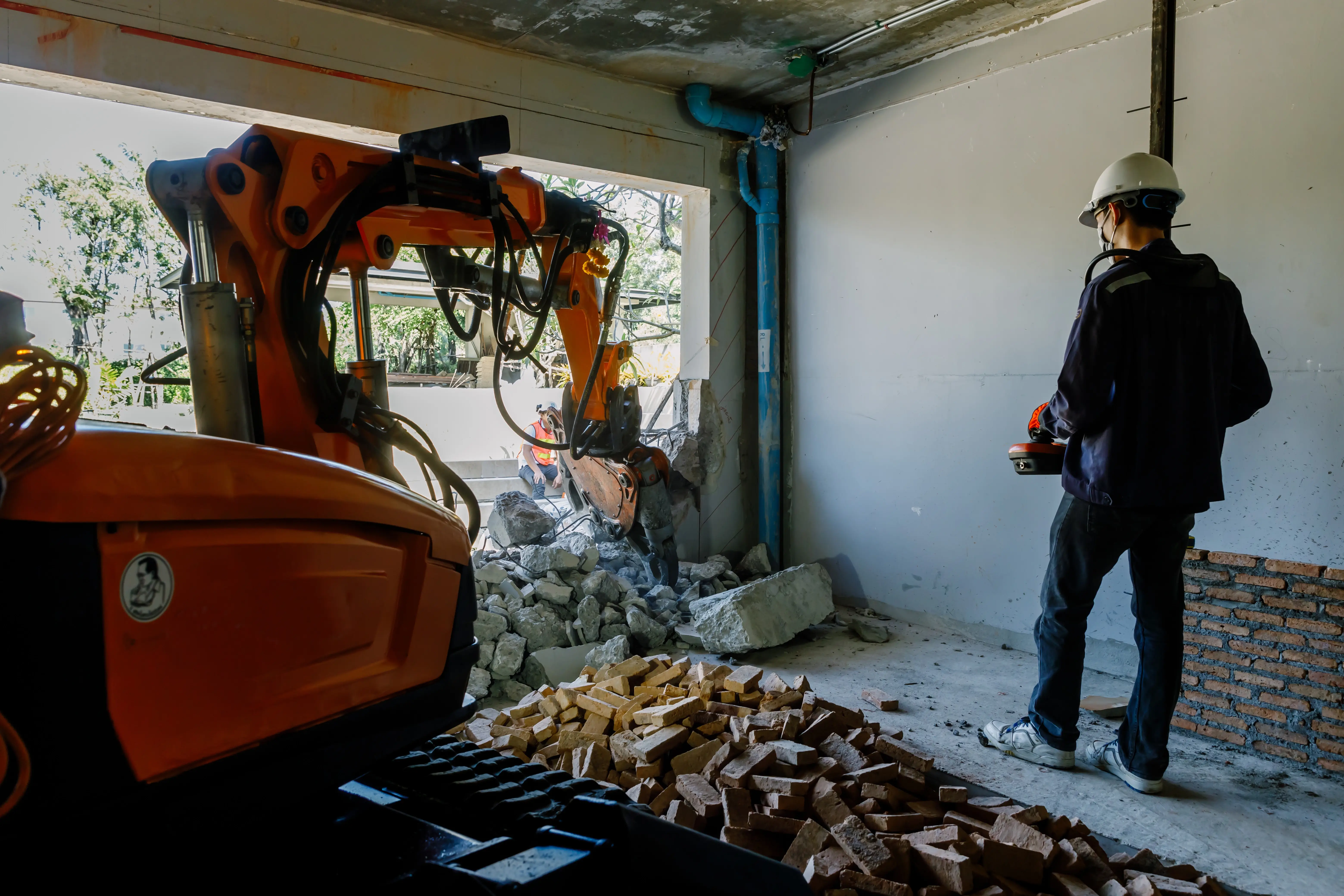 Construction worker supervising a demolition process using an excavator inside a building